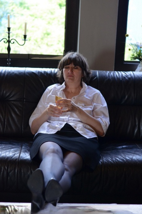 Mature woman exposes her tits and pussy while drinking wine on leather couch