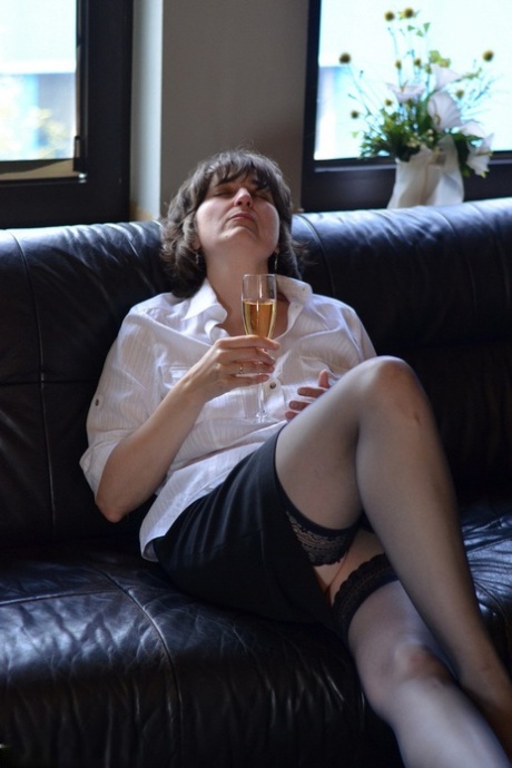Mature woman exposes her tits and pussy while drinking wine on leather couch