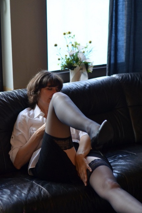 Mature woman exposes her tits and pussy while drinking wine on leather couch